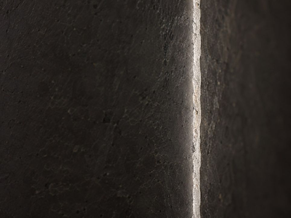 A dark stone field split by one tall pale strip, the sharp edge of a stone blade seen end on.